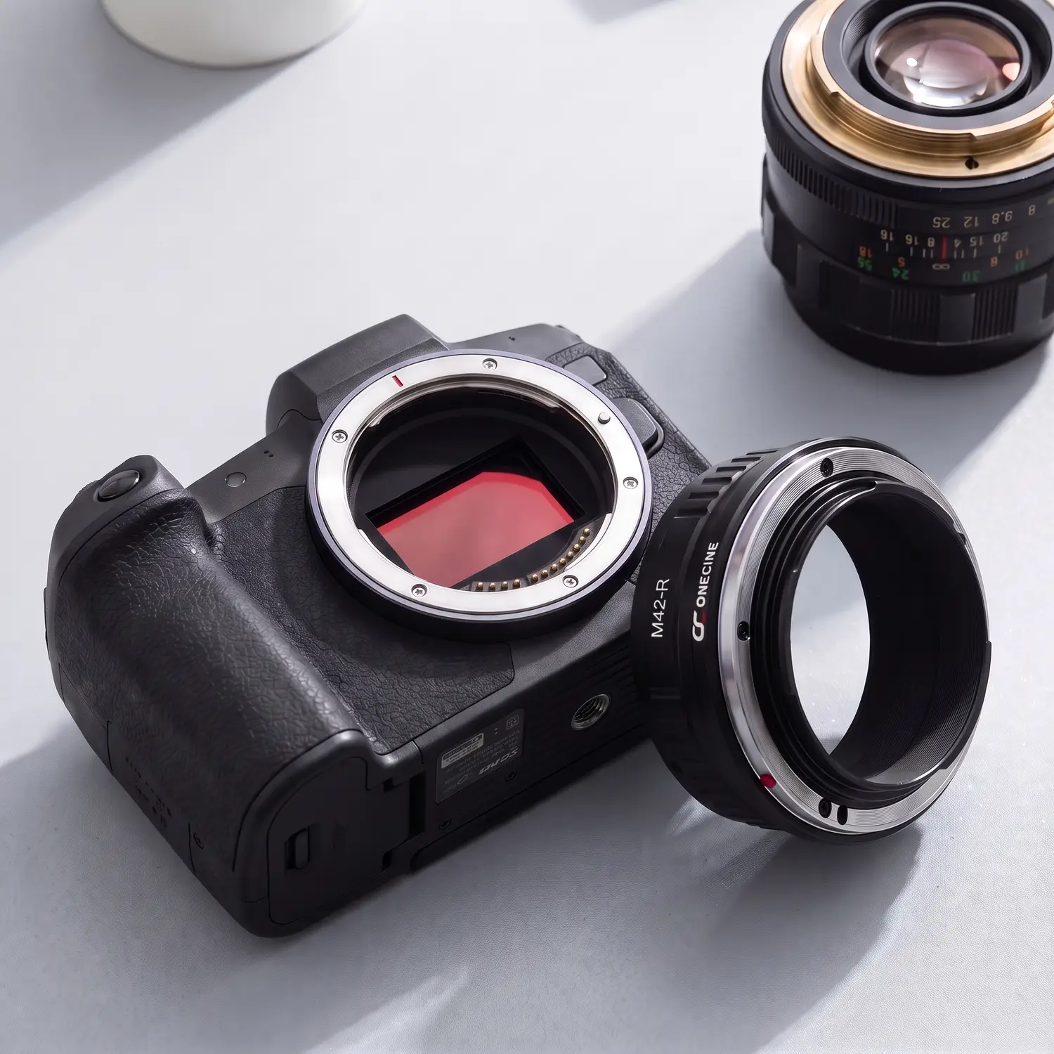 Переходное кольцо OneCine M42-R рядом с байонетом RF камеры Canon и объективом M42
