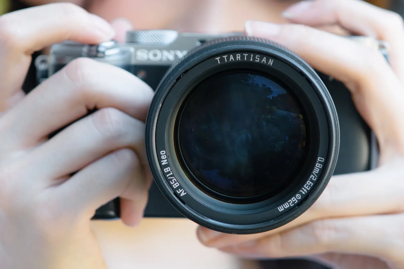Камера Sony с объективом TTArtisan AF 85 мм F1.8 Neo в руках — передняя линза крупным планом