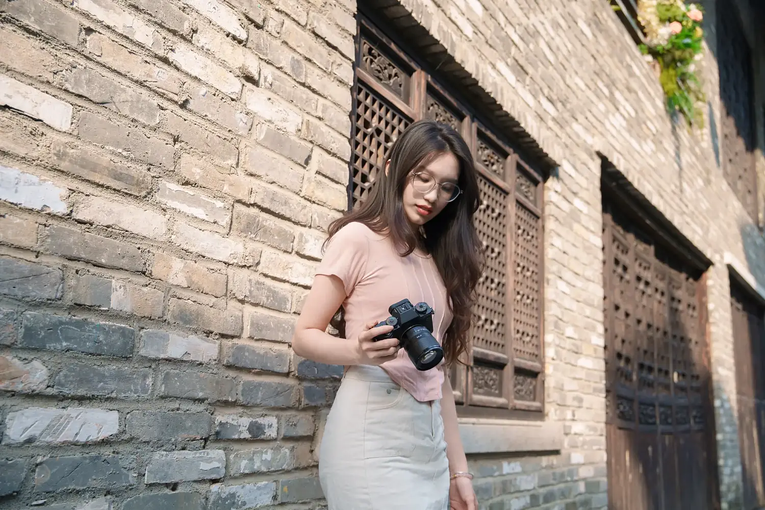 Фотограф с камерой Fujifilm и объективом TTArtisan AF 75 мм F2 у кирпичной стены