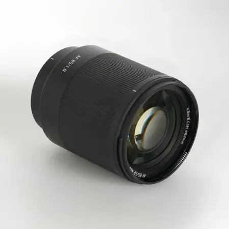 Объектив TTArtisan AF 85 мм F1.8 Neo для Sony E лежит на боку — передняя линза и маркировка 0,8 м / 62 мм