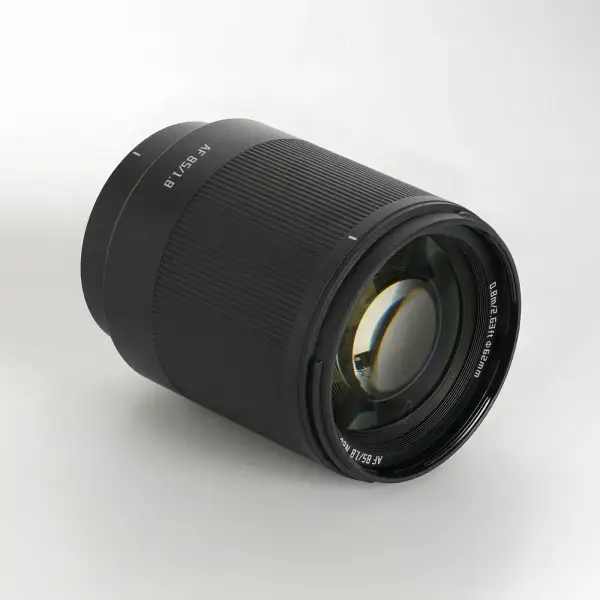 Объектив TTArtisan AF 85 мм F1.8 Neo для Sony E лежит на боку — передняя линза и маркировка 0,8 м / 62 мм